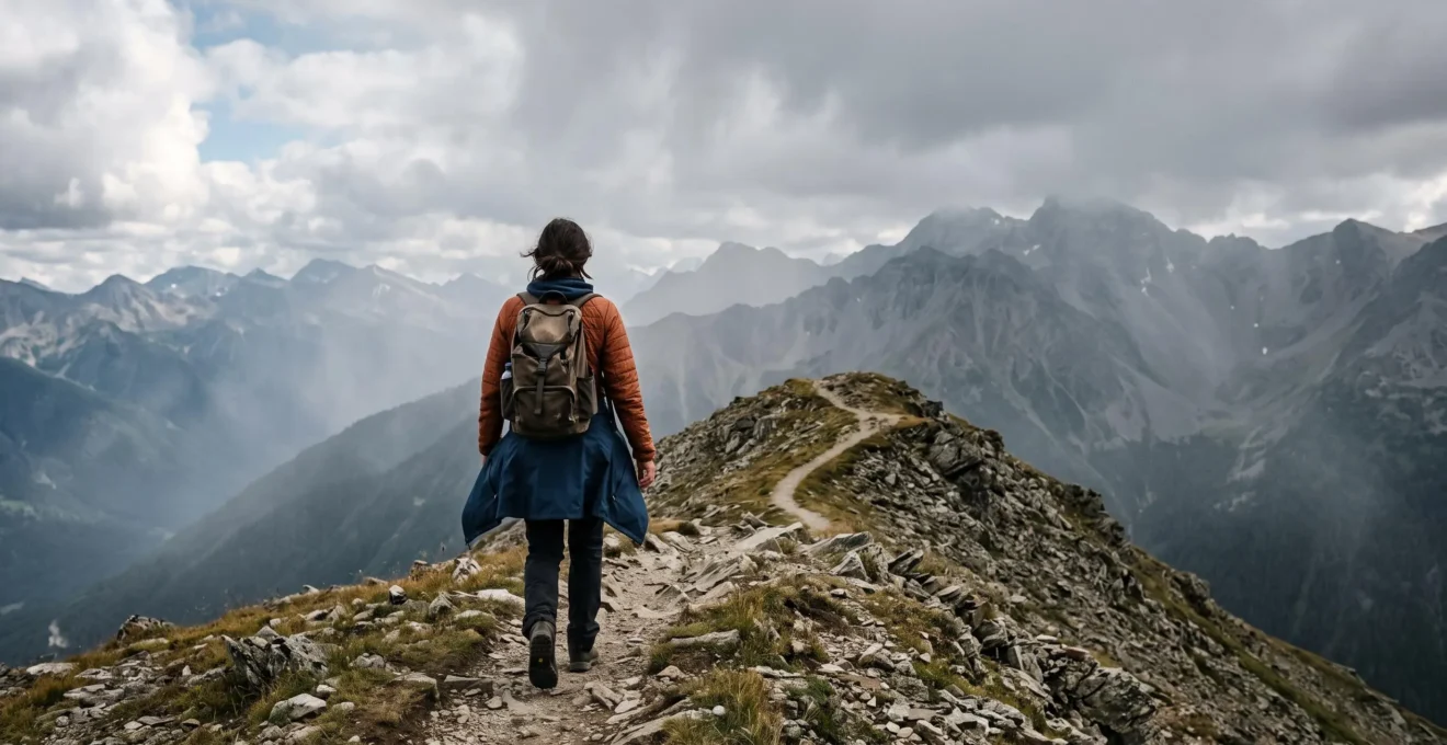 Wanderer in funktionaler Mehrschicht-Kleidung auf einem Bergpfad zwischen Sonne und aufziehendem Nebel